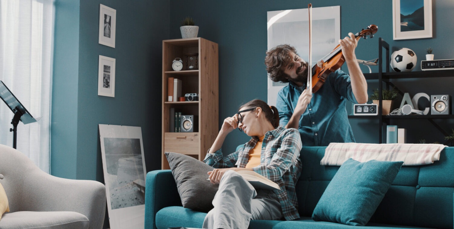 roommate playing violin behind someone on a couch