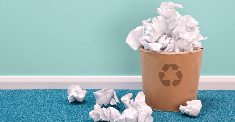 a small brown trash can overflowing with crumpled papers against a teal wall