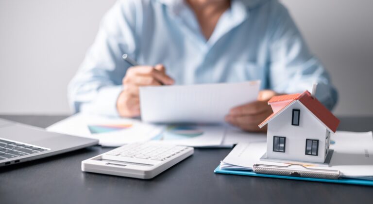 Person sitting at a table with stacked papers and a little house on top of them