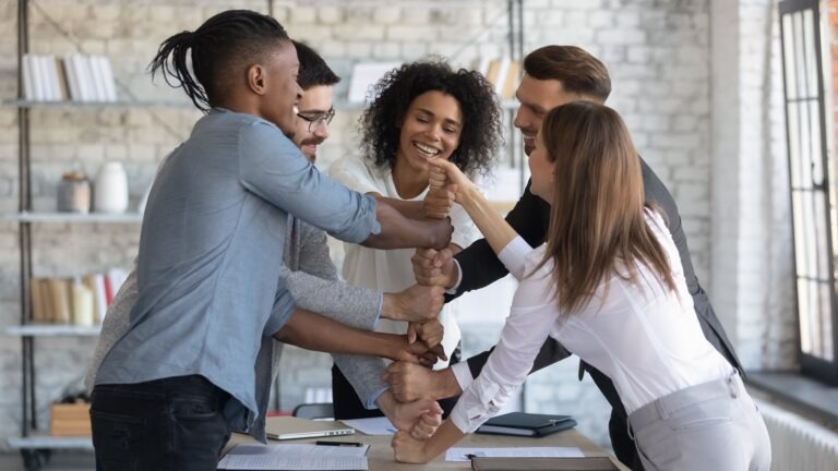 coworkers around a table stacking their fists one upon another