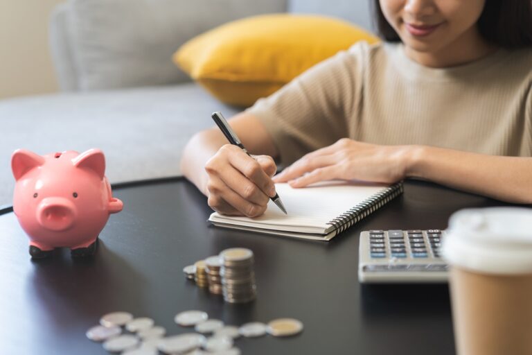 Woman writing notes next to a piggy bank, coins and coffee cup