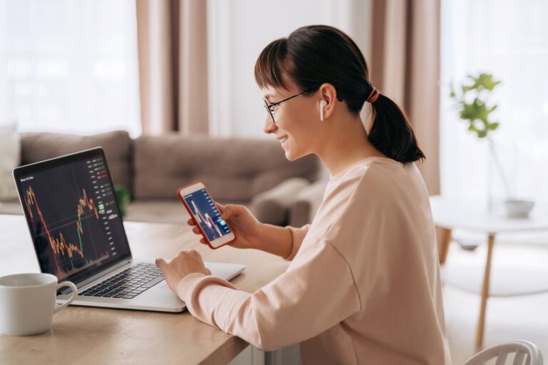 Young woman wearing headphones with phone and computer tracking market trend lines