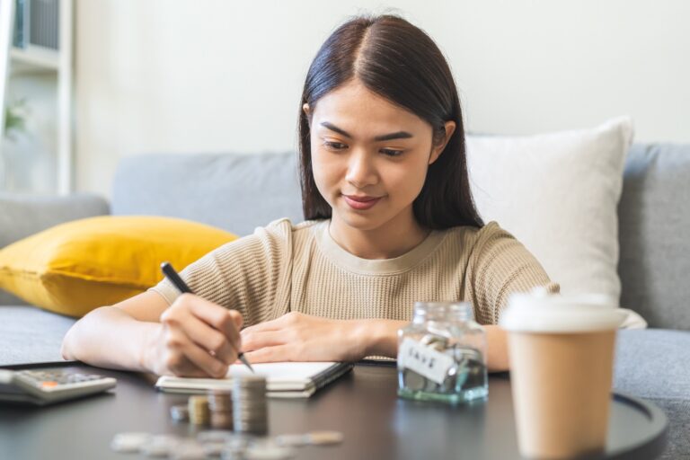 Young woman with pencil and paper, a stack of coins on the table, a cup of coffee