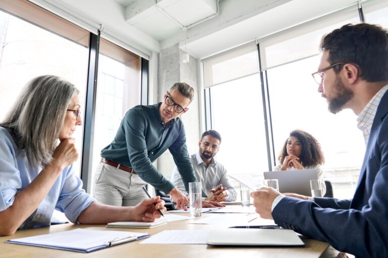 Man in glasses learning over a table full of people