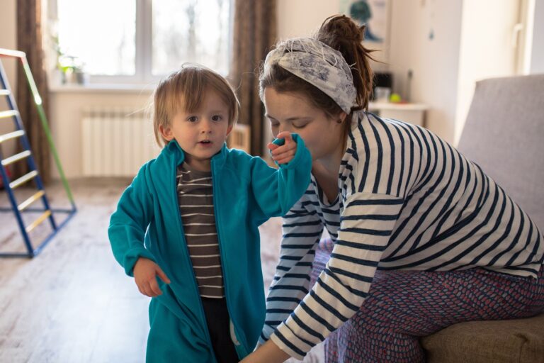 Woman dressing a small toddler in jacket, shirt and jeans