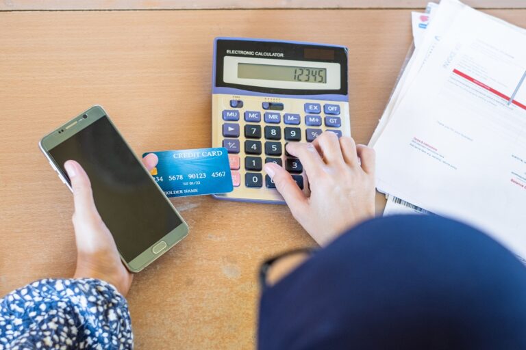 Female hand with cell hone and calculator next to stack of paper bills