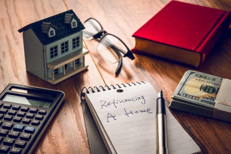 Calculator, toy house, reading glasses and a notepad that says "refinancing a home"