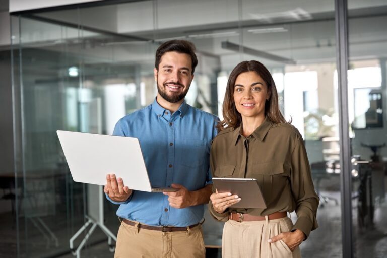 man and woman standing with laptop and ipad smiling